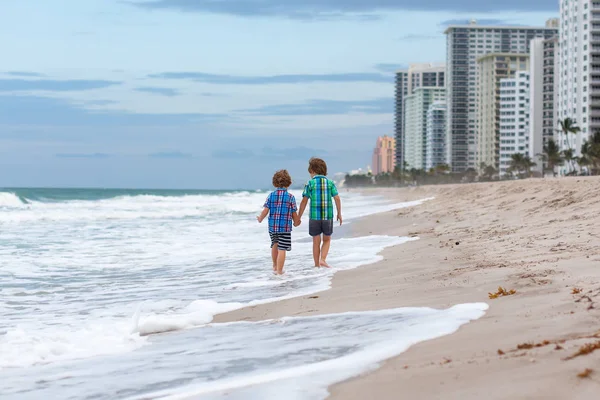 Dos niños felices corriendo en la playa del océano. Divertidos niños lindos, hermanos y mejores amigos haciendo vacaciones y disfrutando del verano en el tormentoso día ventoso en Miami, Florida, Estados Unidos. —  Fotos de Stock