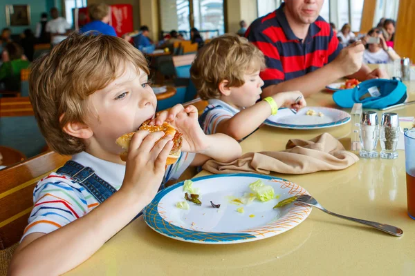 Zwei Vorschulkinder und ein Vater, die im Café auf dem Kreuzfahrtschiff Pasta-Hamburger essen. glückliche Kinder, Zwillinge und Papa essen gesunde biologische und vegane Lebensmittel im Restaurant. Kindheit, Gesundheitskonzept. — Stockfoto