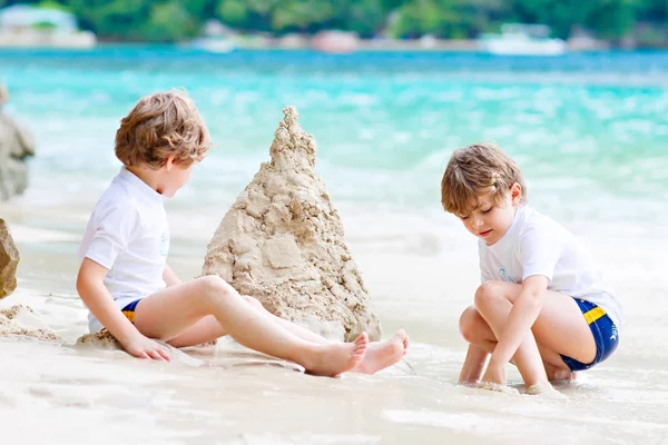 Dos niños pequeños divirtiéndose con la construcción de un castillo de arena en la playa tropical de Seychelles. niños jugando juntos en sus vacaciones — Foto de Stock
