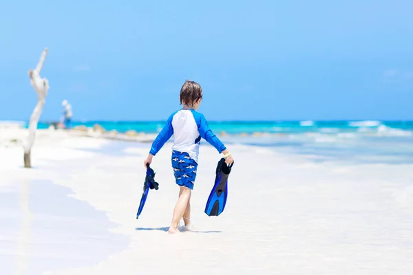 Adorable niño rubio divirtiéndose en la playa tropical de Maldivas. Emocionado niño jugando y surfeando en traje de baño protegido contra el sol en el océano de vacaciones. Arena blanca, niño sosteniendo aletas para nadar —  Fotos de Stock