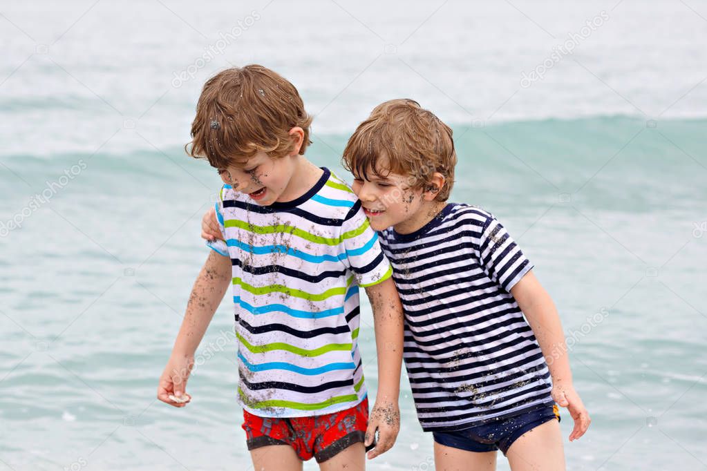 Two happy little kids boys running on the beach of ocean. Funny children, siblings, twins and best friends making vacations and enjoying summer on stormy rainy day. Miami, Florida. Family portrait.