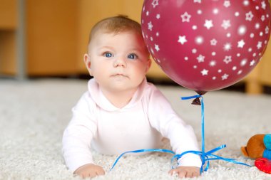 Kırmızı hava balonuyla oynayan şirin bir bebek. Yeni doğmuş çocuk, küçük kız eğleniyor, kavrıyor ve sürünüyor. Aile, yeni hayat, çocukluk, başlangıç konsepti. Bebek yakalama