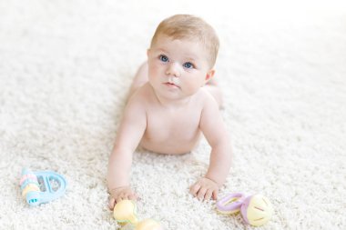Renkli pastel antika çıngıraklı oyuncakla oynayan şirin bir bebek. Yeni doğmuş bir çocuk, küçük bir kız kameraya bakıyor ve emekliyor. Aile, yeni hayat, çocukluk, başlangıç konsepti. Bebek yakalama.