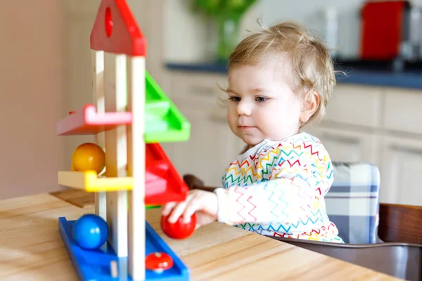 Адекватная симпатичная маленькая девочка, играющая с развивающими игрушками дома или в детском саду. Счастливый здоровый ребенок веселится с разноцветными деревянными игрушечными шариками. Ребенок учится держать и катить мяч . — стоковое фото