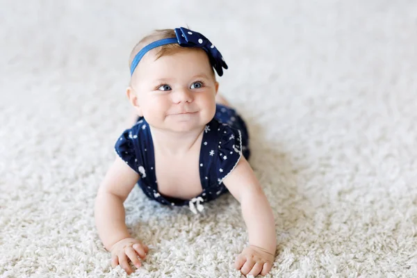 Söt bedårande baby flicka i blå kläder och pannband. lilla barnet tittar på kameran och kryper. Barnet lär sig hastigt på vit bakgrund. Porträtt av glada dotter. Babykläder mode. — Stockfoto