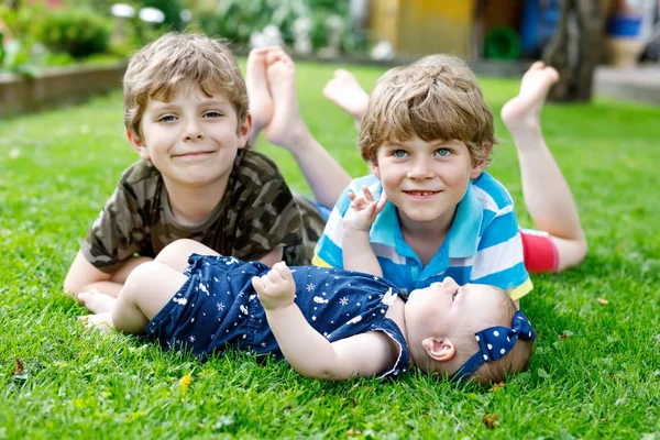 Два маленьких счастливых мальчика с новорожденной девочкой, симпатичная сестра. Братья и сестры на траве летом или весной в саду. Дети сближаются. Семья из трех детей . — стоковое фото