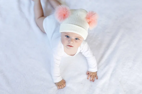 Niedliche entzückende Baby-Kind mit warmen weißen und rosa Hut mit niedlichen Noppen. Glückliches kleines Mädchen, das Krabbeln lernt und in die Kamera schaut. Nahaufnahme für Weihnachtsurlaub und Familienkonzept — Stockfoto
