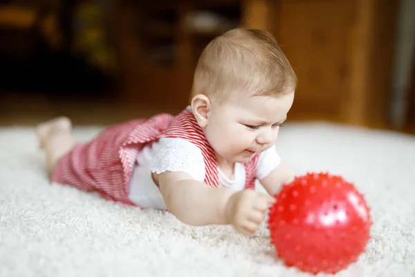 Söt baby leker med röda tuggummi boll. Naturliga flicka tittar på kameran och kryper. Familj, nytt liv, barndom, början koncept. Baby lärande grab. — Stockfoto