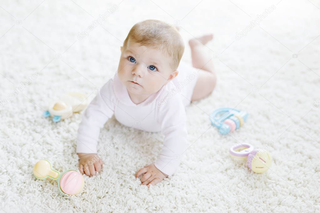 Cute baby playing with colorful pastel vintage rattle toy. New born child, little girl looking at the camera and crawling. Family, new life, childhood, beginning concept. Baby learning grab.