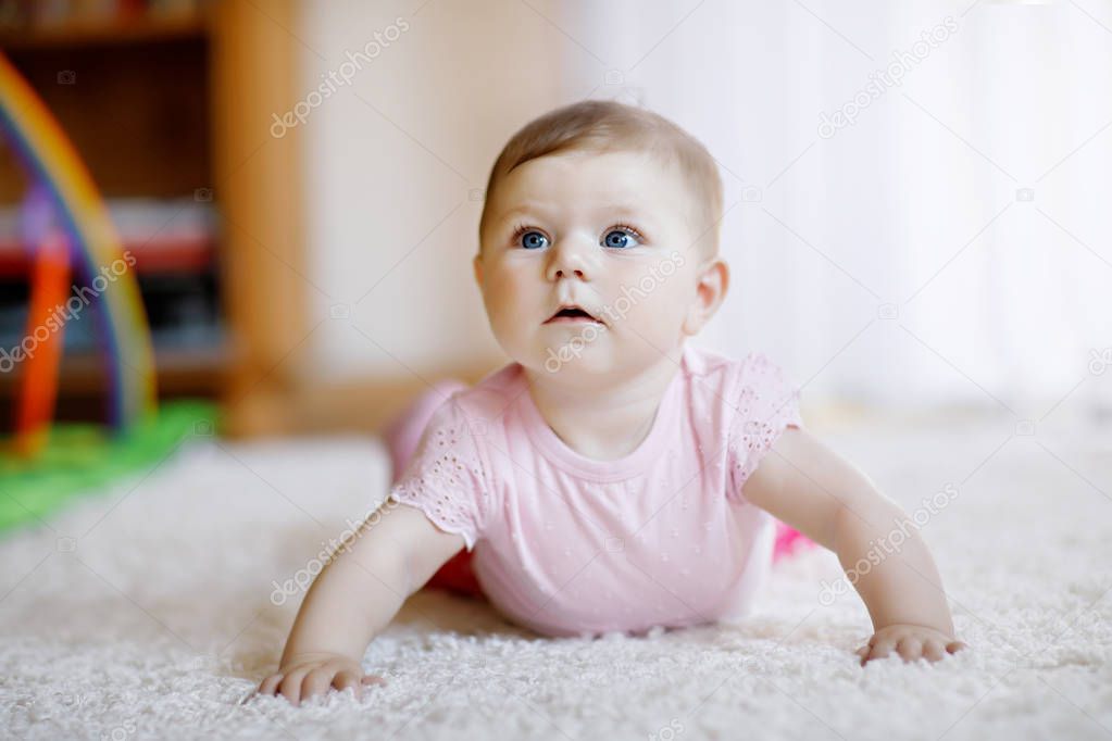 Portrait of baby girl in white sunny bedroom. Newborn child learning crawling. Nursery for children. Textile and bedding for kids. Happy child looking in a camera.