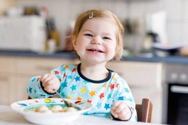 Sevimli bebek kaşık sebze çorbası içiyor. Yemek, çocuk, beslenme ve gelişim konsepti. Sevimli bebek, kaşıklı kız sandalyede oturuyor ve kendi kendine yemek yemeyi öğreniyor..