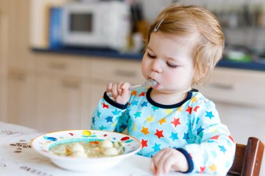 Sevimli bebek kaşık sebze çorbası içiyor. Yemek, çocuk, beslenme ve gelişim konsepti. Sevimli bebek, kaşıklı kız sandalyede oturuyor ve kendi kendine yemek yemeyi öğreniyor..