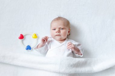 Renkli çıngırak oyuncakla oynamak sevimli yeni doğmuş bebek. evde beyaz yatakta. Yeni doğan çocuk, küçük kız kameraya sürpriz arıyor. Aile, yeni bir hayat, çocukluk, başlangıç kavramı.