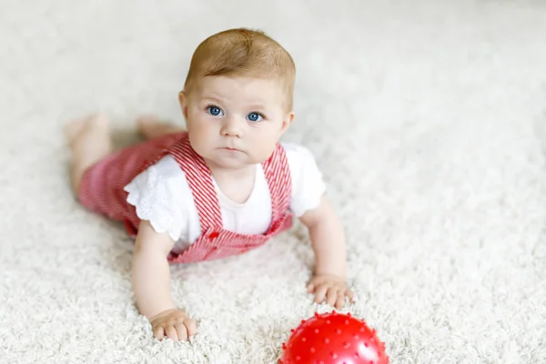 Schattige baby spelen met red gum ball. Lttle meisje kijkend naar de camera en kruipen. Familie, nieuw leven, kindertijd, begin concept. Baby leren pak. — Stockfoto