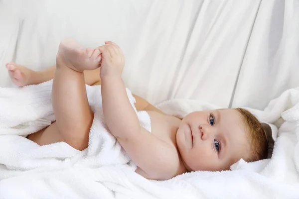 Lindo bebé jugando con sus propios pies después de tomar el baño. Adorable hermosa chica envuelta en toallas blancas. Feliz bebé sano —  Fotos de Stock