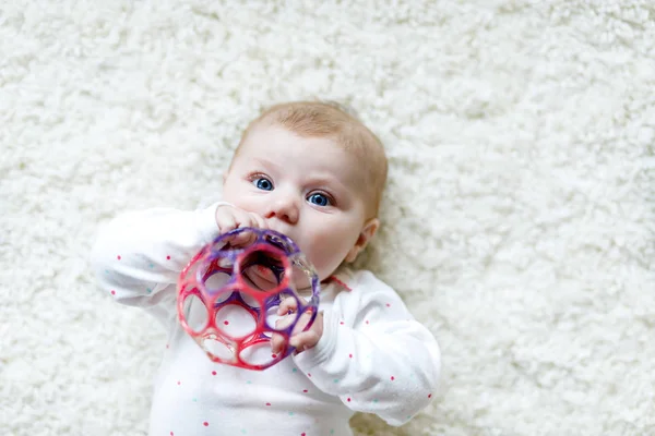 Симпатичный обожаемый новорожденный малыш, играющий с разноцветной гремучей игрушкой на белом фоне. Новорожденный ребенок, маленькая девочка смотрит в камеру. Семья, новая жизнь, детство, начало концепции. Детский захват . — стоковое фото