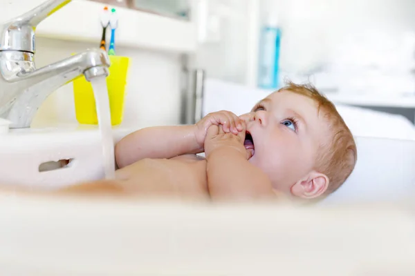 洗面台でお風呂に入り、水汲みをしている可愛い赤ちゃん。大きな青い目の小さな健康的な女の子が楽しんでいます。きれいな美しい子供の遊び — ストック写真