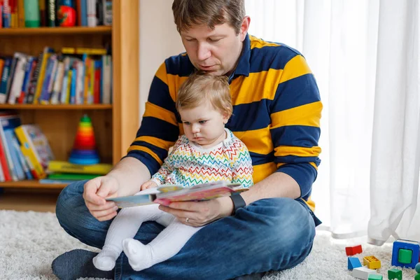 Ung far läser bok med sin söta söta lilla dotter flicka. Le vackert barn och man sitter tillsammans i vardagsrummet hemma. Leksaksförhör med pappa. — Stockfoto