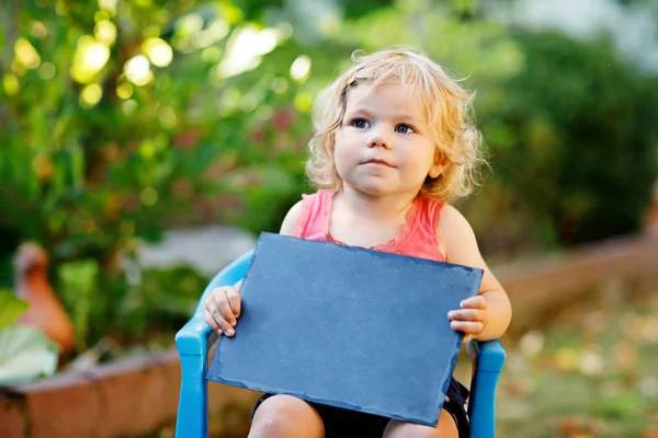 Glad liten toddler flicka med krita skrivbord i händerna. Friska bedårande barn utomhus tomt skrivbord för copyspace innehav av vacker baby. — Stockfoto