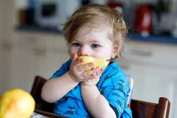 Menina adorável bonito bebê comendo pêra fresca. Criança feliz com fome de um ano segurando frutas. Menina na cozinha doméstica, tendo refeição saudável lanche. Criança loira sorridente — Fotografia de Stock