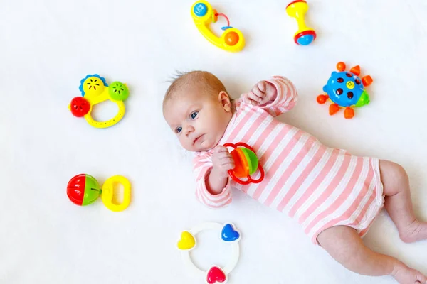 Carino adorabile neonato che gioca con il giocattolo colorato sonaglio. in letto bianco a casa. Bambino appena nato, bambina che guarda sorpresa la macchina fotografica. Famiglia, nuova vita, infanzia, concetto iniziale . — Foto Stock