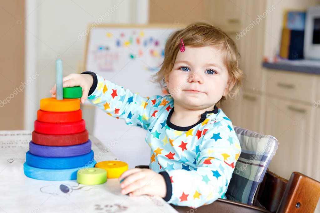Adorable cute beautiful little baby girl playing with educational toys at home or nursery. Happy healthy child having fun with colorful wooden rainboy toy pyramid. Kid learning different skills.