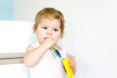 Küçük kız diş fırçası tutuyor ve ilk dişlerini fırçalıyor. Bebek süt dişini temizlemeyi öğreniyor. Önleme, hijyen ve sağlık hizmetleri kavramı. Banyoda mutlu bir çocuk..