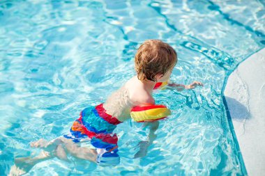 Mutlu küçük çocuk çocuk yüzme havuzuna eğleniyor. Yüzmeyi öğrenme etkin mutlu bir çocuk. güvenli floaties veya swimmies ile. Aile, tatil, yaz konsepti