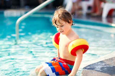 Mutlu küçük çocuk çocuk yüzme havuzuna eğleniyor. Yüzmeyi öğrenme etkin mutlu bir çocuk. güvenli floaties veya swimmies ile. Aile, tatil, yaz konsepti