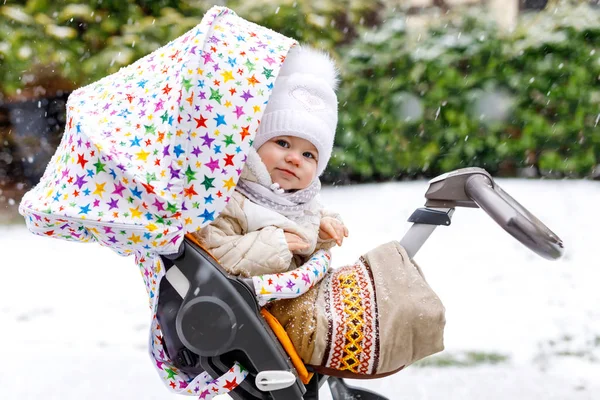 Bonita menina bonita sentada no carrinho de bebê ou carrinho no dia frio com mangas, chuva e neve. Criança sorridente feliz em roupas quentes, moda casaco de bebê elegante. Bebê com guarda-chuva grande. — Fotografia de Stock