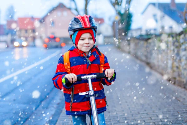 Leuke kleuter die op een scooter naar school rijdt. activiteiten voor kinderen in de buitenlucht in de winter, lente of herfst. grappig vrolijk kind in kleurrijke mode kleding en met helm. Hoge snelheid. — Stockfoto