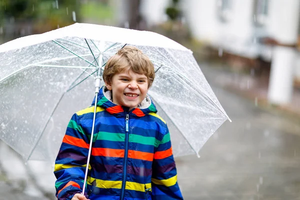 Hermoso niño en camino a la escuela caminando durante el aguanieve, la lluvia y la nieve con un paraguas en el día frío. Niño feliz y alegre en ropa casual de moda colorida. — Foto de Stock