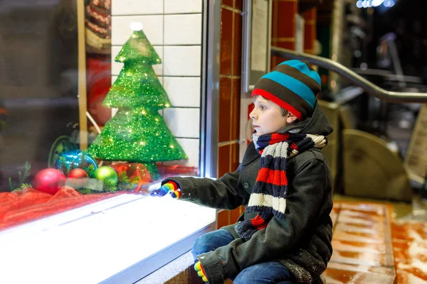 かわいい学校の子供男の子クリスマス マーケットに。ウィンドウ ショッピング ファッション冬服で面白い幸せな子はギフト、クリスマス ツリーで飾られました。祝日、クリスマス、幼年期および人々 の概念.. — ストック写真