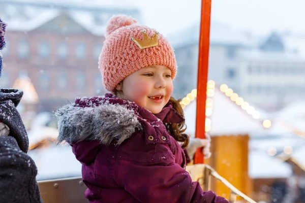 Pequeña niña linda que se divierte en la rueda del hurón en el mercado tradicional alemán de Navidad durante las fuertes nevadas . — Foto de Stock