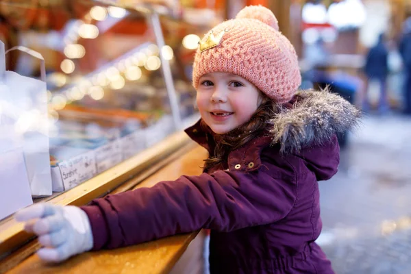 Pequeña niña linda cerca de soporte dulce con manzanas azucaradas y frutas de chocolate. Niño feliz en el mercado de Navidad en Alemania. Ocio tradicional para familias en Navidad. Fiesta, celebración, tradición . — Foto de Stock