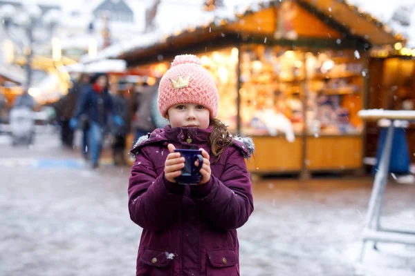 Niña linda con taza de chocolate caliente al vapor o ponche para niños. Niño feliz en el mercado de Navidad en Alemania. Ocio tradicional para familias en Navidad . — Foto de Stock
