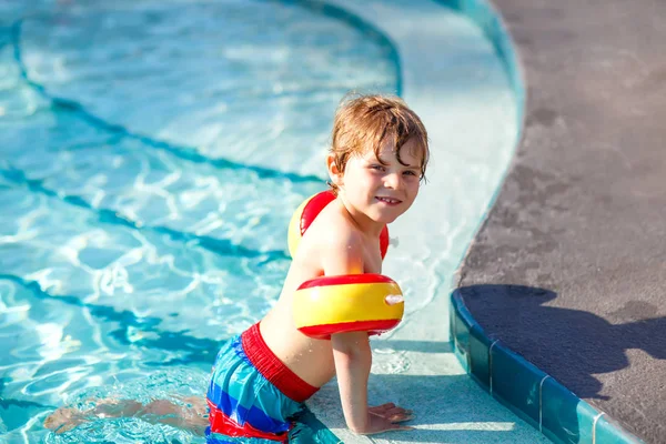 Šťastné dítě chlapec baví v plaveckém bazénu. Aktivní šťastné dítě naučit se plavat. s bezpečnou floaties nebo swimmies. Rodina, dovolená, letní koncepce — Stock fotografie