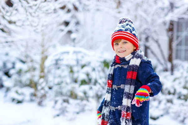 Roztomilé malé zábavné dítě v barevné zimní módní oblečení baví a hrát si se sněhem, venku během sněžení. Aktivní venku volný čas s dětmi. Kluk a batole chytají sněhové vločky. — Stock fotografie