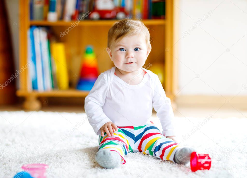 Adorable baby girl playing with educational toys in nursery. Happy healthy child having fun with colorful different toys at home. Baby development and first steps, learning to play and to grab.