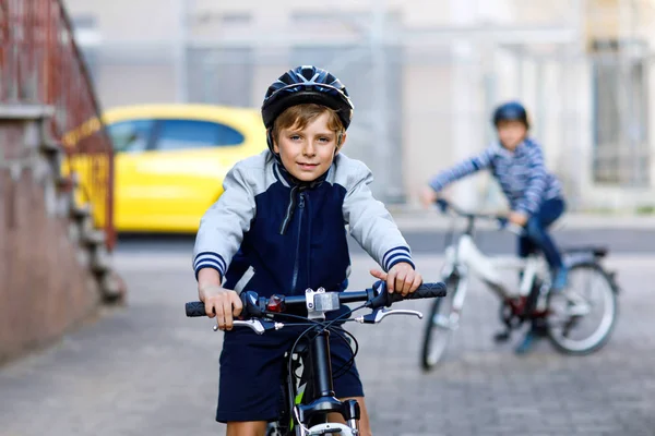 Two school kid boys in safety helmet riding with bike in the city with backpacks. Happy children in colorful clothes biking on bicycles on way to school. Safe way for kids outdoors to school — Stock Photo, Image