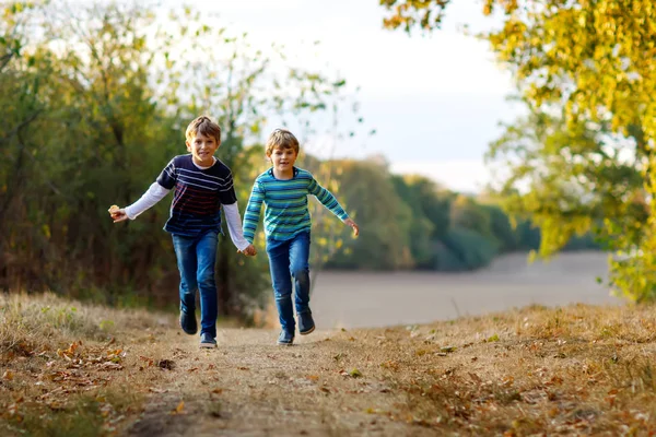 Zwei kleine Schulkinder rennen und springen im Wald. fröhliche Kinder, beste Freunde und Geschwister, die sich an einem warmen, sonnigen Frühherbsttag vergnügen. Zwillinge und Familie, Natur und aktive Freizeit. — Stockfoto