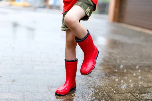 เด็กใส่รองเท้าบูทฝนสีแดง กระโดดลงไปในสระน้ํา . — ภาพถ่ายสต็อก