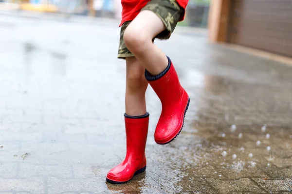 Kind in roten Regenstiefeln springt in eine Pfütze. — Stockfoto