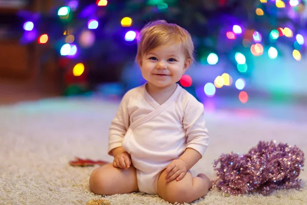 かわいい赤ちゃん女の子かわいい手でカラフルなライト ガーランドを保持します。お祝いで子供服を飾るクリスマス ツリー — ストック写真
