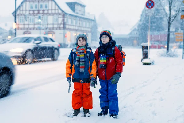 Dos niños pequeños de la clase primaria caminando a la escuela durante las nevadas —  Fotos de Stock