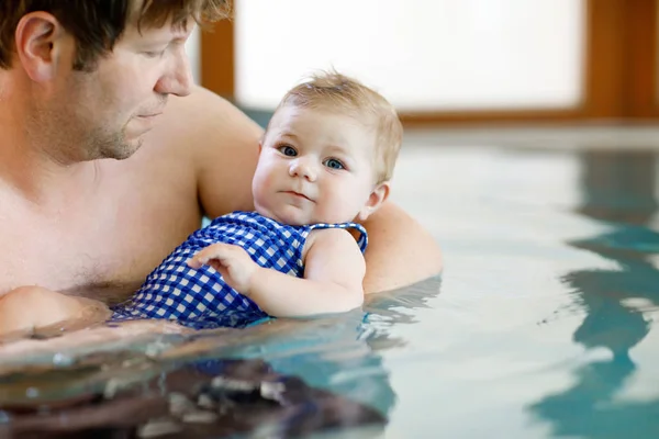 Happy middle-aged father swimming with cute adorable baby girl in swimming pool.