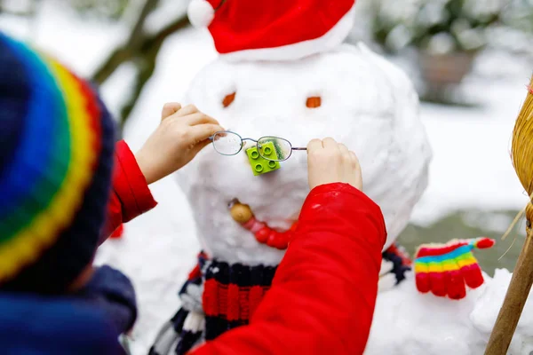Little kid putting eye glasses on snowman. Close-up. child having fun with first snow in winter — Stock Photo, Image