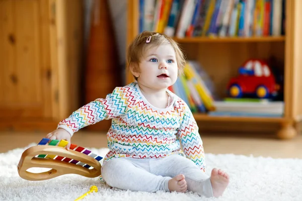 Адекватная симпатичная маленькая девочка, играющая с развивающими деревянными музыкальными игрушками дома или в детском саду. Тоддлер с красочным ксилофоном — стоковое фото