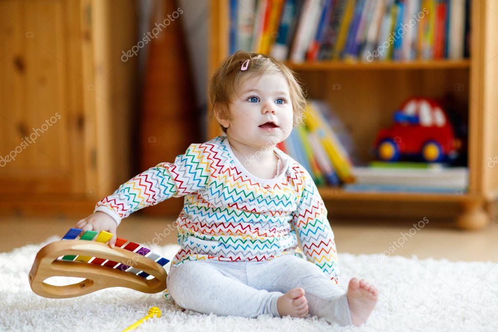 Adorable cute beautiful little baby girl playing with educational wooden music toys at home or nursery. Toddler with colorful xylophon