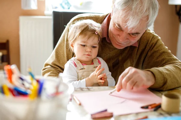 Cute little baby toddler girl and handsome senior grandfather painting with colorful pencils at home. Grandchild and man having fun together — Stock Photo, Image